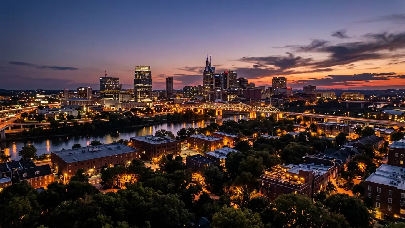 A dramatic dusk view of the Nashville skyline with warm lights over rooftops and trees